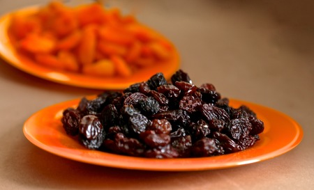 dry apricots and dry black grapes on orange glass plates - it is tasty and beautifulの写真素材