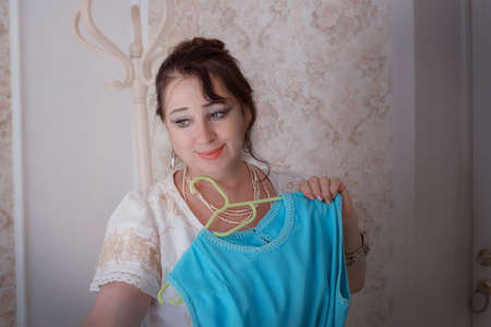 a woman with black hair holds a blue dress in her hands.