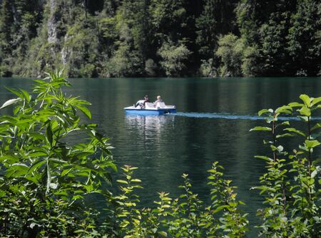 Wonderful beauty of great Nature of Germany. Mountain lake Alpsee with blue-green turquoise colored clean deep water. A couple riding on catamaran, leaving a trail on the water. Moments of journey.の写真素材