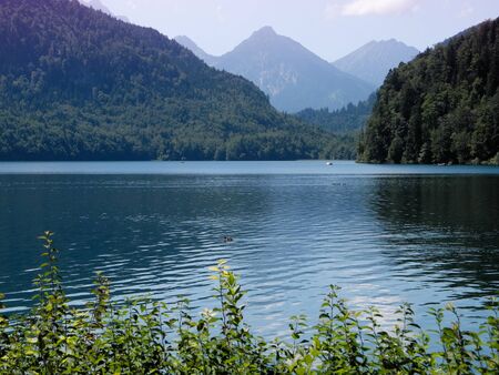 Wonderful beauty of great Nature of Germany. Mountain lake Alpsee with blue-green turquoise colored clean deep water. Smoky purple mountains on horizon.の写真素材