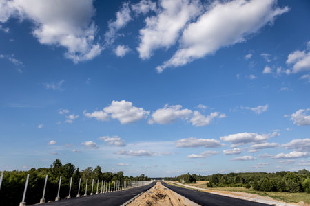 Asphalt road under blue sky with white clouds in the countryside.