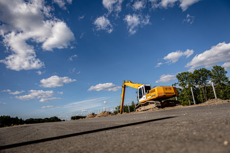 excavator on a road construction site with blue sky and white cloudsの写真素材