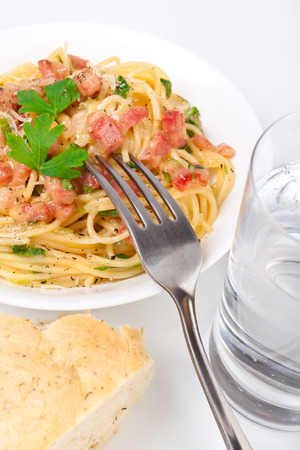 one serving of traditional spaghetti carbonara with a glass of water, a fork and a piece of breadの写真素材
