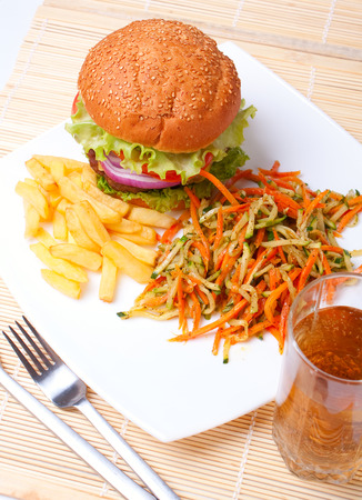 a big cheeseburger with a small portion of french fries and fried healthy vegetables and a glass of ice teaの写真素材