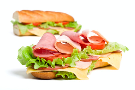 two halves of long baguette sandwich with lettuce, tomatoes, ham, turkey breast and cheeseの写真素材