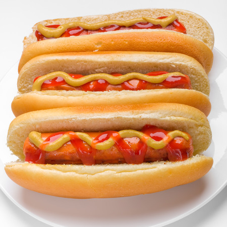 three classic hotdogs with mustard and ketchup on a plateの写真素材