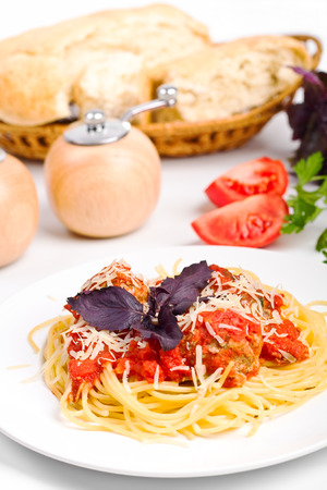 one serving of spaghetti bolognese with tomatoes, a salt shaker, a pepper box and foccacia bread in the backの写真素材