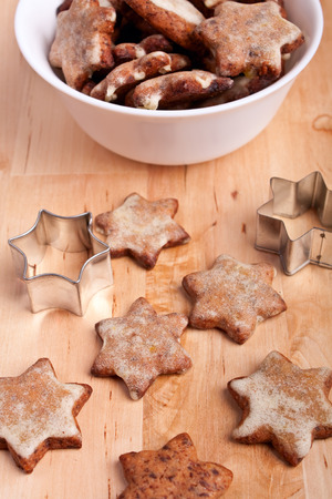 homemade star-shaped christmas cookies with a star cookie-form on a wooden board with more cookies in a bowl at the backの写真素材