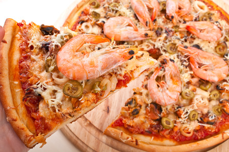 whole seafood pizza sliced with one slice liftedの写真素材