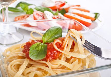 linguine with tomato sauce and green basil and caprese salad at the backの写真素材