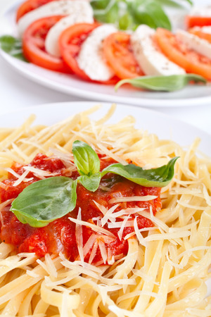 Linguine pasta with tomato sauce, cheese and basil and caprese salad in the backの写真素材