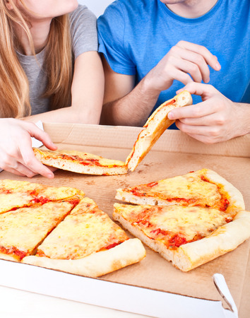 two young people eating pizza from a boxの写真素材