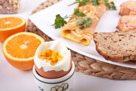 breakfast meal with a cheese omelett, boiled egg, oranges and ham and cheese toastsの写真素材
