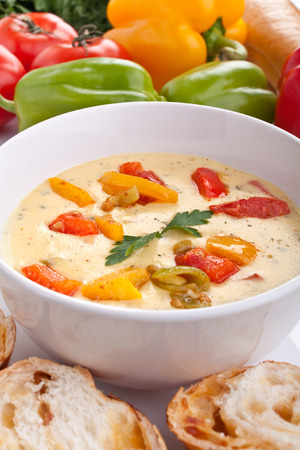 serving of cheese and vegetable cream soup with ingredients at the backの写真素材