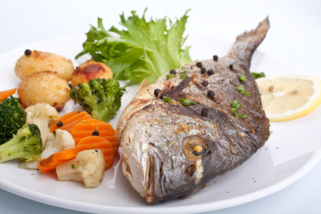 Sea Bream fish with vegetables on white plate close-upの写真素材