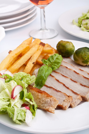 sliced pork chops with french fries, brussels sprouts and wineの写真素材