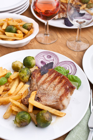 two servings of pork chops with fries and brussels sprouts and red wineの写真素材