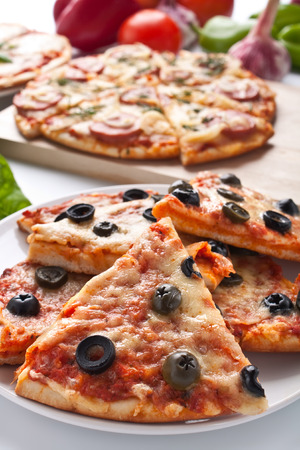 sliced sausage and black olive pizzas with ingredientsの写真素材