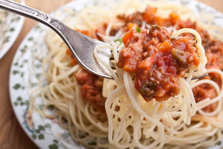 spaghetti bolognese on a fork and a big plate of spaghettiの写真素材