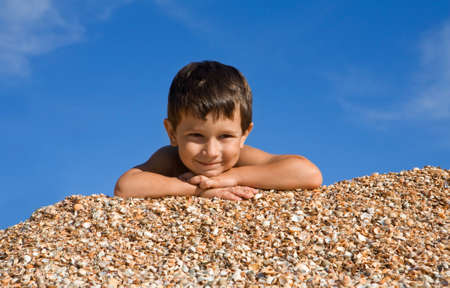 Happy boy lying on shells and looking at camera with smile on hot summer dayの写真素材