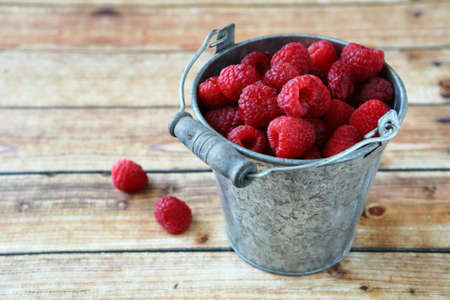 Fresh raspberries in a small bucket on wooden boards