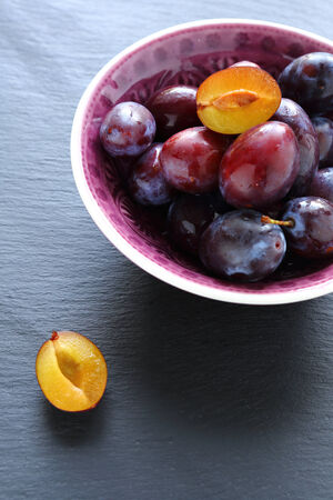 Ripe plums in a bowl on slate background, delicious foodの写真素材