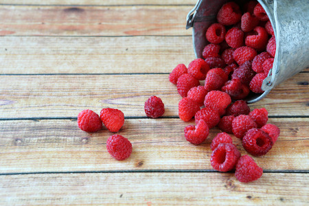 Delicious raspberries in a small bucket,  wooden background
