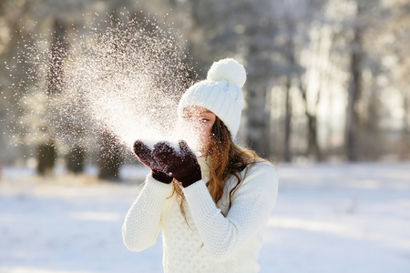 Woman blowing in the snow in his hands, outdoors in winterの写真素材