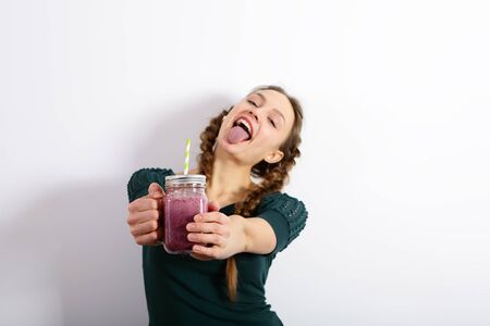 Cheerful young woman showing tongue, holding smoothie in the hands