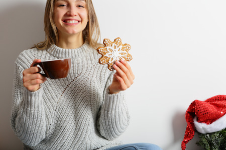 Beautiful smiling young woman drinks cocoa with ginger Christmas cookies, looks at the camera