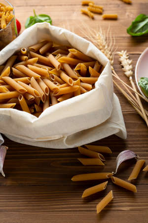Whole grain uncooked pasta penne in cotton bag close upの写真素材
