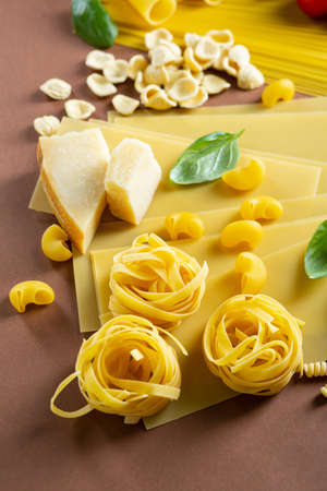 Italian pasta types background with cheese and green basil leaves on brown surfaceの写真素材
