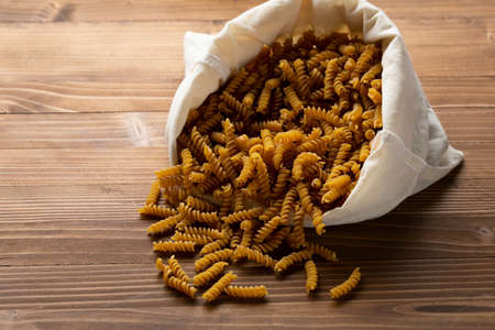 Whole wheat pasta in cotton storage bag on wooden tableの写真素材