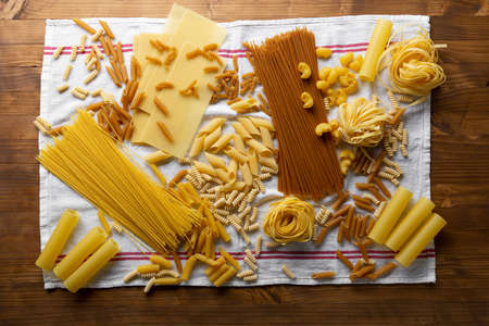 Overhead view of Different types of pasta on white textile on wooden tableの写真素材
