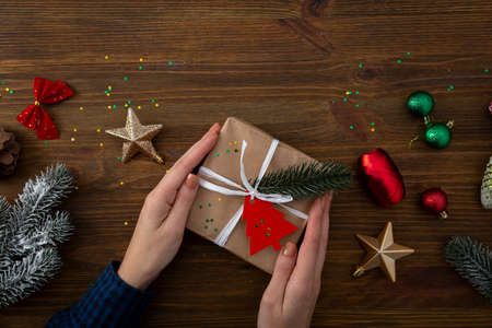 Wooden background with Christmas decorations and small gift box in handsの写真素材