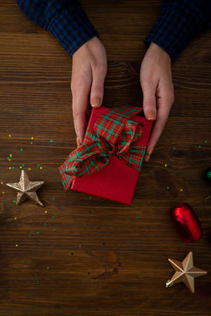 Red gift box in hands and Christmas decorations on wooden surfaceの写真素材