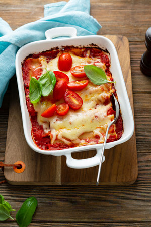Baked canneloni in white baking dish on wooden tableの写真素材