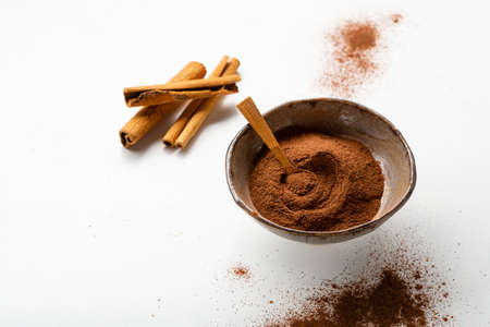 Cinnamon sticks and powder in bowl white surface copy space