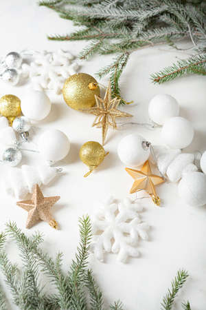 Golden and white Christmas tree decorations on light surface and green branchesの写真素材