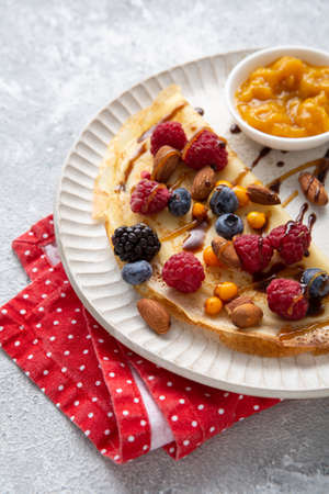 Close up of crepes with berries and sauce on white plateの写真素材