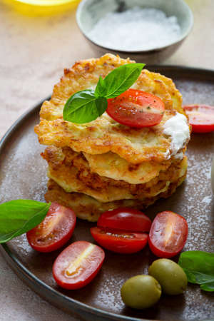 Stack of potatoes fritters served with cherry tomato and olive on plateの写真素材