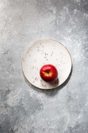 One Red apple on plate on gray concrete surfaceの写真素材