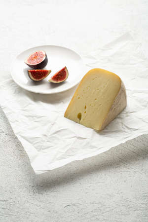 One cheese piece on wrapping paper and figs fruits food on light surfaceの写真素材