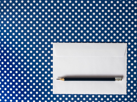 White paper envelope and black pencil on a blue background polka dot. Top View.