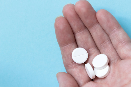 Female hand whire circle pills. Blue background. Medications. Concept medicine