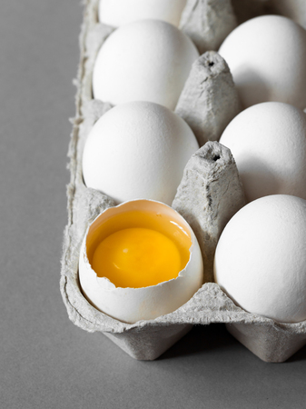Close up broken egg yolk in carton packing on gray background. Vertical photo