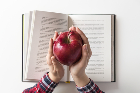 Girl student holding red apple over open book on white table. Education concept.の写真素材