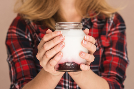 A young woman in a plaid shirt is holding a jar with sweet homemade yogurt with berry jamの写真素材