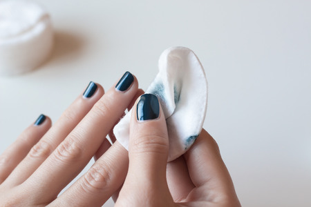 Woman removes the nail polish. Hands with dark blue manicure on whote table.の写真素材