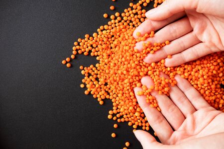 Woman hands and red lentils on black background